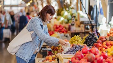 Woman is chooses fruits and vegetables at food market. Reusable eco bag for shopping. Sustainable lifestyle. Eco friendly concept.