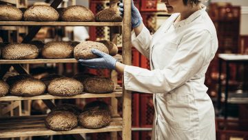 Young female worker working in bakery. She puts bread on shelf.
