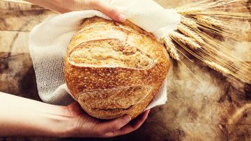 Baker holding a loaf of bread on rustic bacgkround