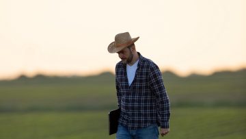 Farmer walking in soy field carrying laptop