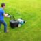 Gardener in the garden mows grass with a lawn mower. Side view