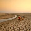 Young man sitting on boat at drying river. Drought impact and Climate change
