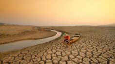 Young man sitting on boat at drying river. Drought impact and Climate change