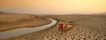 Young man sitting on boat at drying river. Drought impact and Climate change