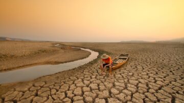 Young man sitting on boat at drying river. Drought impact and Climate change