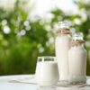 Glass and bottles of fresh milk on table outdoors